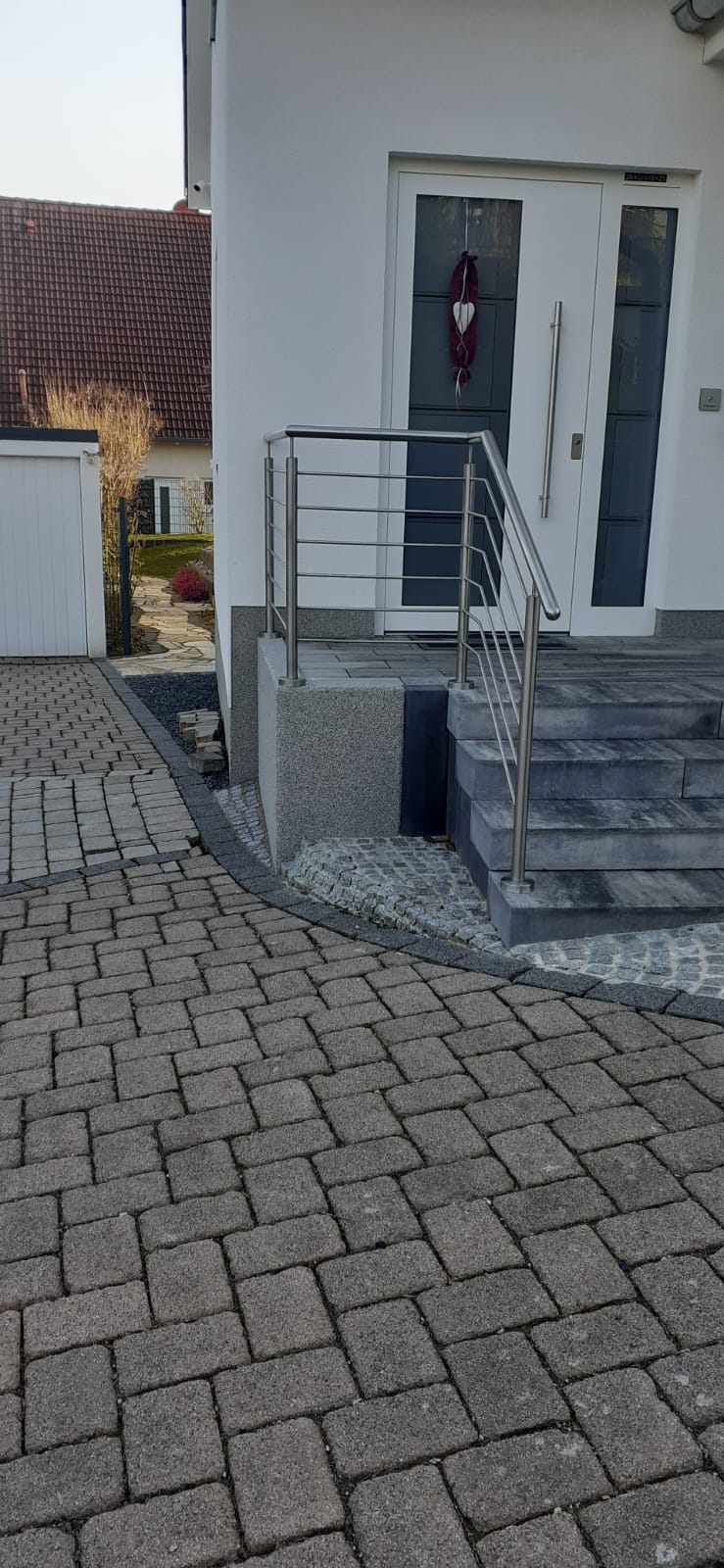 Eingangsbereich eines weißen Hauses mit grauen Stufen und Edelstahlgeländer